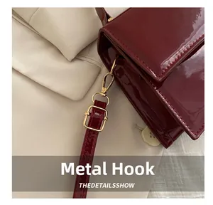 Detail of wine red patent leather handbag with shiny gold metal hook and strap hardware
