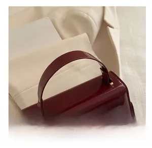 Close-up of deep red glossy patent leather handbag with a sleek arched top handle