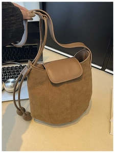 Close-up of brown suede bucket bag featuring drawstring details and round ball ornaments