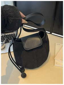Detail of black suede bucket bag featuring drawstring closure and leather handle