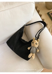 Detailed view of black suede hobo bag with a cute plush rabbit charm on a white sofa