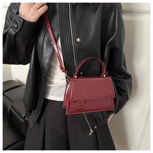 Detail of a deep red patent leather handbag featuring a glossy finish and long strap