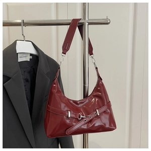 Close-up of burgundy patent leather shoulder bag with metallic buckle on gray suit
