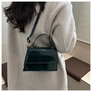 Dark green patent leather crossbody bag shown on model wearing a grey wool coat