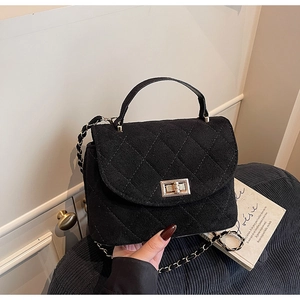 Close-up of elegant black quilted suede handbag with gold metal twist lock and chain strap