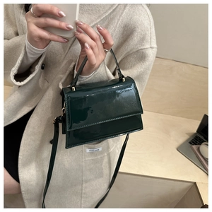 Detail of dark green patent leather handbag with gold hardware and top handle