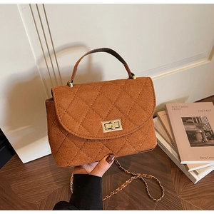 Detail of brown suede quilted handbag with golden rotary lock and chain strap in soft light