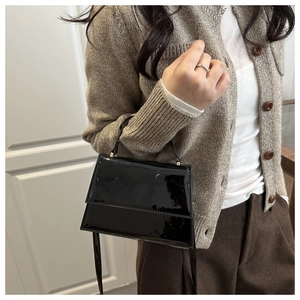 Detail of black patent leather crossbody bag showing glossy texture and top handle
