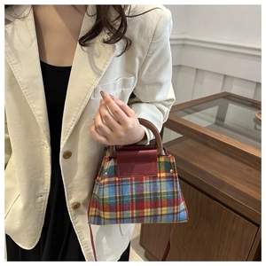 Detail of tartan plaid handbag with wooden handles and red leather flap closure on a model