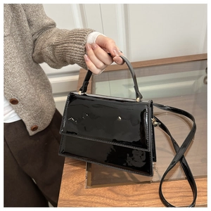 Detail of glossy black patent leather handbag with top handle and stylish metal buckle
