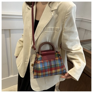 Detailed view of British plaid fabric texture and red faux leather strap on handbag