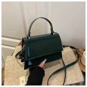 Macro view of dark green patent leather handbag with glossy texture and gold hardware