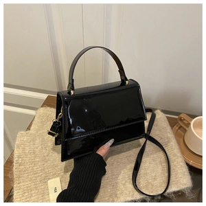 Close-up of black patent leather crossbody bag on a cozy knitted mat with home decor