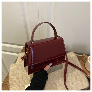 Detail of burgundy patent leather handbag with gold hardware on beige knitwear