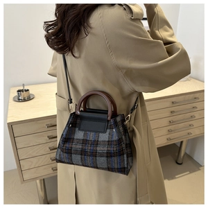 Detail of vintage plaid wool tote with elegant curved wooden handle on camel coat