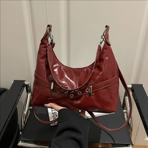 Glossy dark red underarm bag with silver buckle strap on a sleek half-moon silhouette