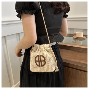 Détail d'un sac seau en paille tressée beige avec logo en cuir marron et cordon serrage
