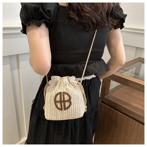 Détail du sac seau en paille tissée avec logo HB en cuir marron et cordon sur mannequin