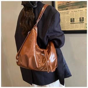 Gros plan d'un sac hobo en cuir PU marron brillant porté avec un blazer rétro