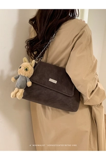 Detail of dark brown matte leather crossbody bag with metal chain strap and plush rabbit toy