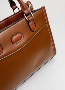 Detail of brown leather tote showing fine texture, black edge paint and gold metal hardware