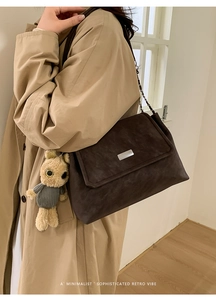 Detail of dark brown suede shoulder bag with silver buckle and cute teddy bear charm