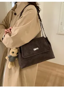 Detail of a coffee brown large tote bag with bear charm on a beige trench coat