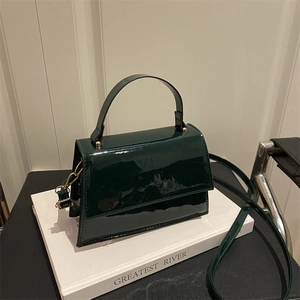Vintage dark green patent leather handbag with gold hardware on a white art book