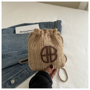 Détail du sac porte-bonheur en paille tressée avec logo HB en cuir marron et cordon