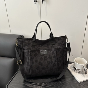 Large black floral canvas tote bag with fashion tag and detachable strap on desk