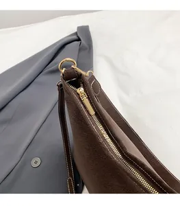 Détail du sac bandoulière en daim marron foncé avec fermeture éclair dorée et coutures