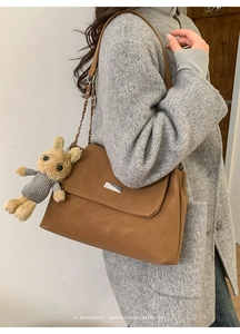Detailed side view of a brown faux leather shoulder bag with metal buckle and plush bunny charm