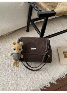 Detail of dark brown tote bag with silver chain strap and plush animal charm on a chair