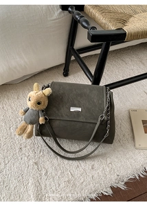 Detail of dark gray matte bag with silver buckle and plush rabbit charm on a rug
