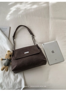 Deep brown matte shoulder bag with silver bar and teddy bear charm on white fabric