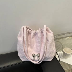 Sac à épaule plissé rose avec nœud argenté et cordon sur un canapé en cuir noir