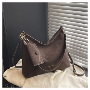 Détail d'un sac hobo marron avec mini pochette et garniture dorée sur un tissu blanc