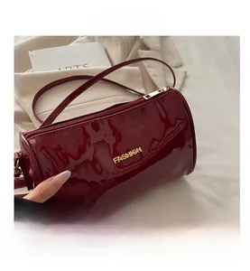 Gros plan du sac cylindre en cuir verni bordeaux avec lettrage fashion en métal doré
