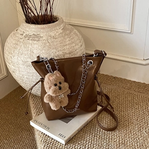 Chic brown glossy chain bucket bag with plush dog charm on art magazine background