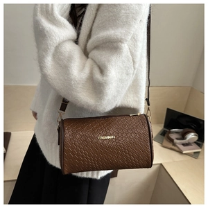 Détail d'un sac cylindre marron à texture tressée avec logo doré et finitions élégantes