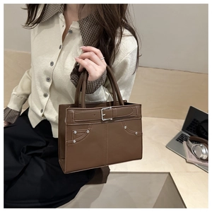 Detail van een donkerbruine leren shopper met gespen en zilveren klinknagels op een bureau