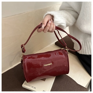 Détail du sac polochon en cuir verni bordeaux avec logo doré et poignée élégante