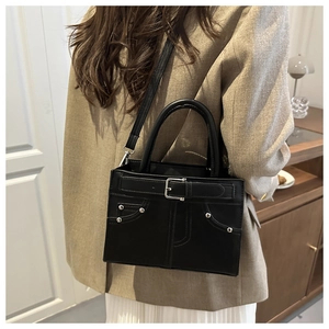 Detail of black tote bag featuring decorative buckles and metal rivets on soft leather