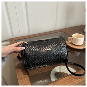 Détail d'un sac cylindrique noir matelassé avec logo doré et fine bandoulière en cuir