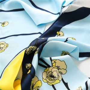Détail d'un foulard en soie montrant le tissu bleu clair et les motifs floraux jaunes