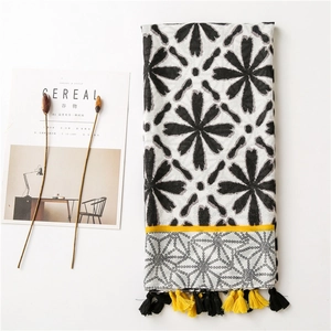 Detail of floral linen shawl with black flower patterns and yellow tassel trim
