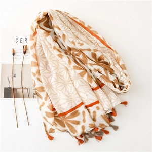 Detail of white scarf with brown abstract patterns, orange stripes, and tassel accents