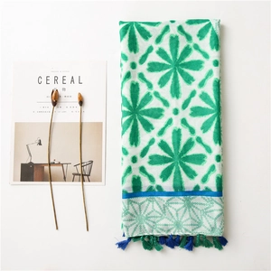 Detail of floral printed linen scarf with vibrant blue and green tassels on white background