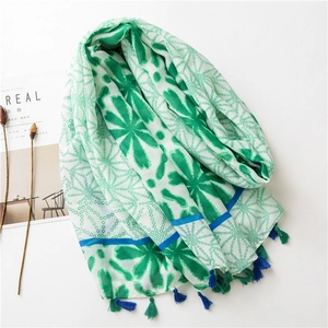 Detail of a white summer scarf with green floral patterns and colorful tassel edges