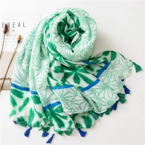 Detail of printed scarf with green leaves, blue lines, and two-tone decorative tassels